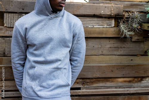 Midsection of african american man wearing grey hooded sweatshirt against wooden fence, copy space