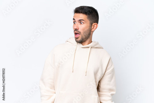 Young caucasian man isolated on white background doing surprise gesture while looking to the side