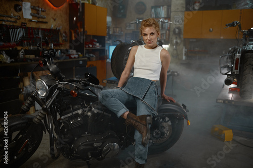 Beautiful woman biker sitting on motorcycle in garage