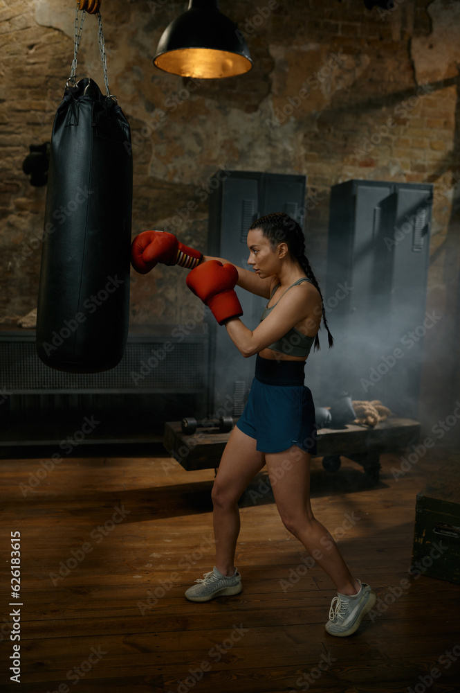 Strong girl fighter boxing with punching bag having workout training