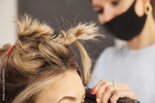 Barber shop. Close-up of hairdresser female making hairdress for cute young lady in barbershop room. Customer service in hair salon, create doing. Concept of hairstyle, hair care. Copy ad text space