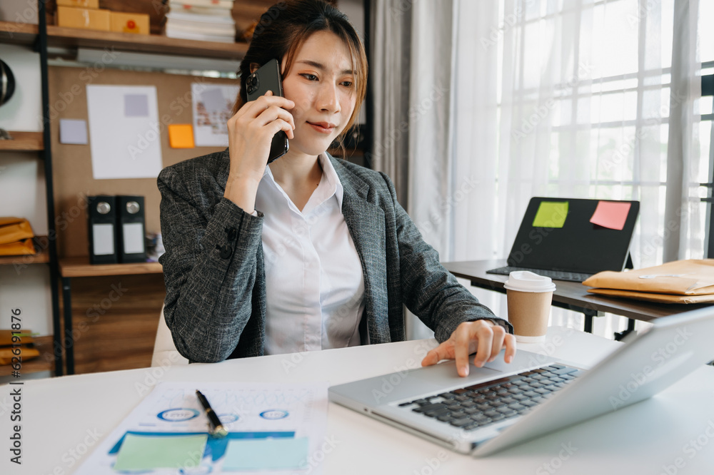 Business asian woman Talking on the phone and using a laptop with a smile while sitting at office. Business asian woman Talking on the phone and using a laptop with a smile while sitting at office.