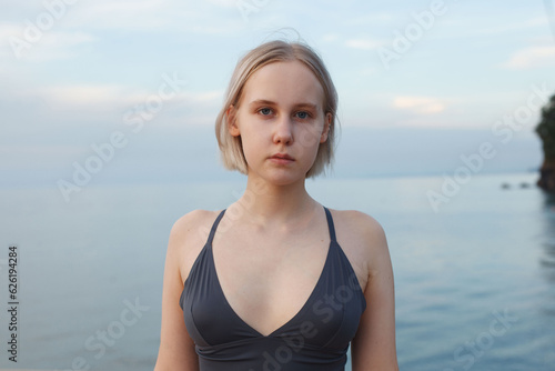 Portrait of short-haired blonde woman standing on the background of blue sea and sky full of clouds