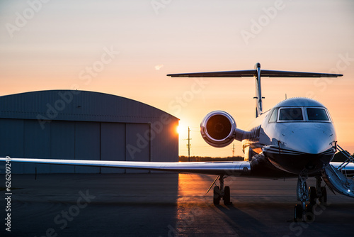 Private jet on tarmac at sunrise with stairway deployed and hangar in background