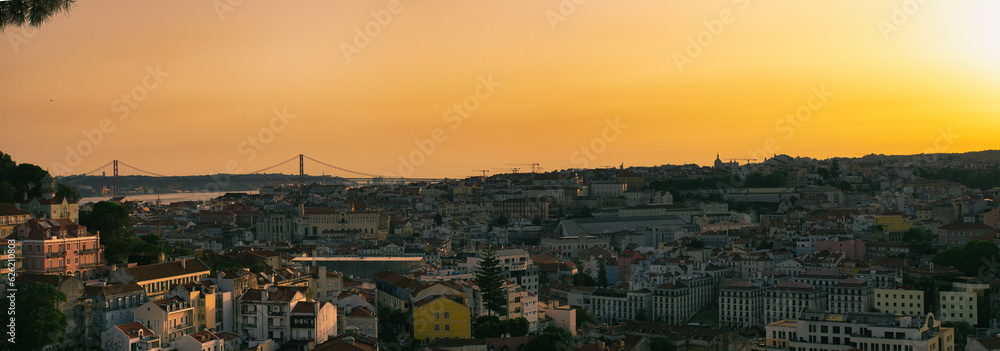 A breathtaking panoramic view of Lisbon at sunset, captured from the Miradouro da Nossa Senhora do Monte. The city’s vibrant colors and historic architecture are beautifully illuminated by the warm gl