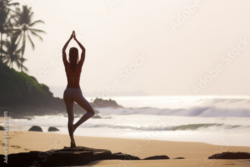 A woman practices yoga on a tropical beach. Back view.