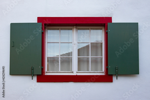 Picturesque window with open shutters on white wall of house, Swiss heritage, downtown. Discreet, laconic style of Switzerland in dark red and green colors