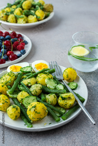 Delicious lunch or dinner, boiled young potatoes with asparagus beans and young fresh cucumbers, boiled eggs and fresh berries, refreshing water with lemon and mint