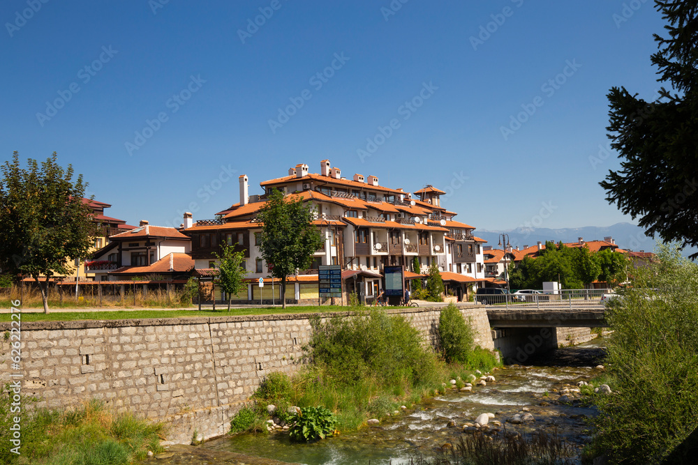 View of Bansko town, bulgarian ski resort in summer, Pirin Mountains on the background, a river on the foreground, Bulgaria.