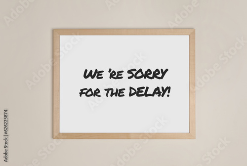 Frame with phrase We're Sorry For The Delay on beige wall