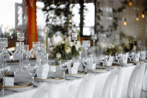 фотографія Wedding decor, table setting with white dishes, glass glasses and flowers, against the background of lanterns