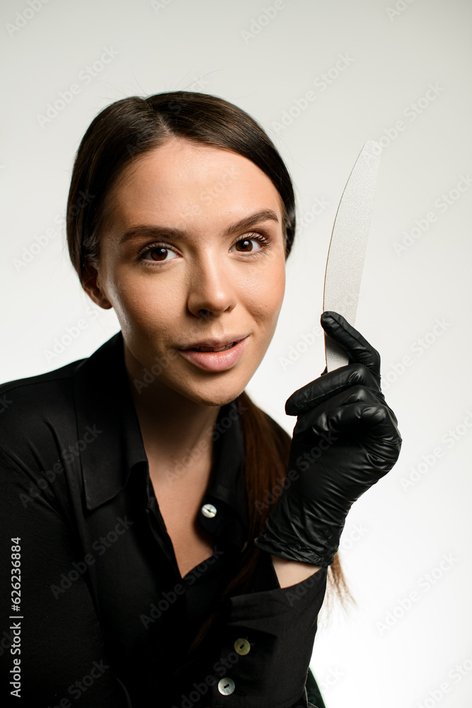 Portrait of woman nails artist in black uniform with nail file in hand on white background Portrait of woman nails artist in black uniform with nail file in hand on white background