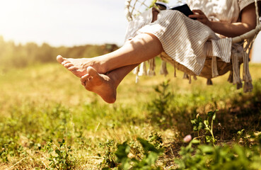 Women legs, barefoot girl sitting on swings in nature, outdoor on summer holiday
