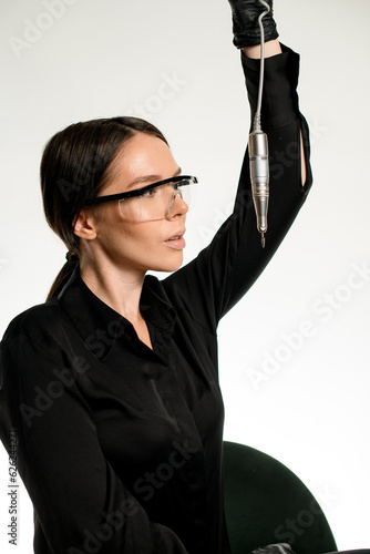 Woman master of nails in black uniform with protective glasses on her face holds frazer for manicure in hand photo