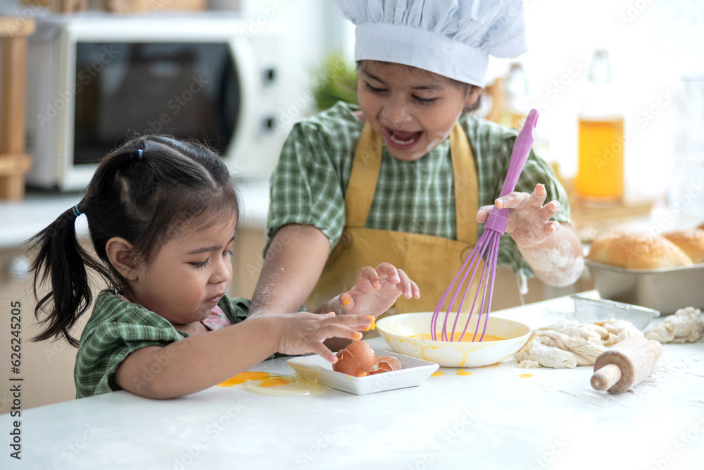 Two sisters enjoy preparing breakfast in the kitchen, younger sister helped break an egg to make an omelet
