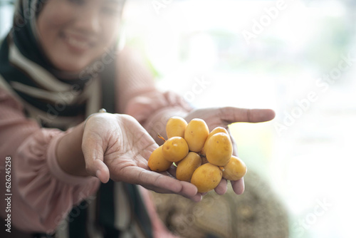 Muslim woman showing yellow date palms in hands, yellow Bahi dates farm produce, sweet and delicious for eating fresh, selective focus photo