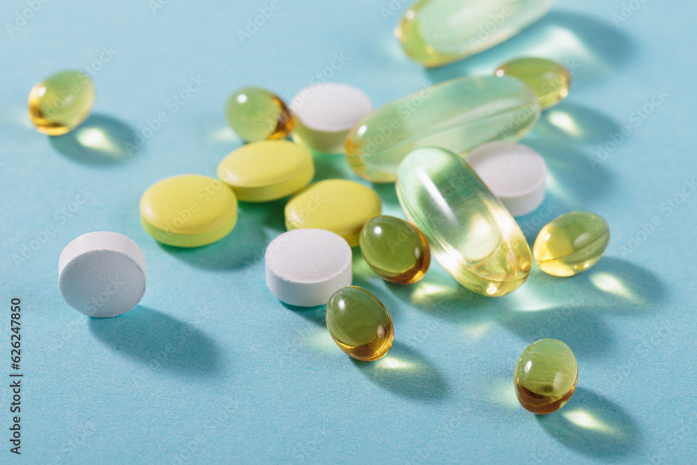 Diet, nutrition, healthy eating concept. Assorted Oil filled yellow softgels capsules and pills of food supplements on light blue background Diet, nutrition, healthy eating concept. Assorted Oil filled yellow softgels capsules and pills of food supplements on light blue background