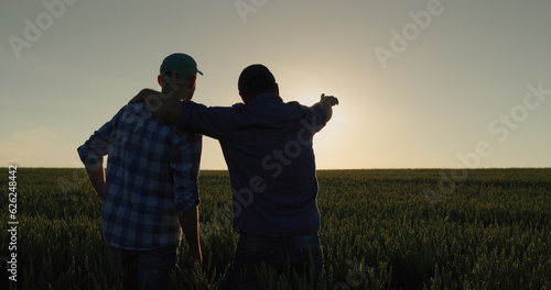 A man and his son watch the sunrise over a wheat field together. Farmers in the field and family business