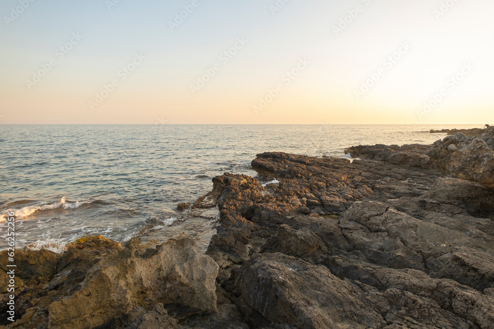 Sunset over tranquil beach with rocky cliffs, clear sky, and calm water