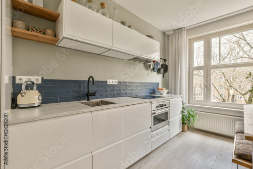 a kitchen with blue tiles on the backs and white cabinets  along with an open window looking out onto the street