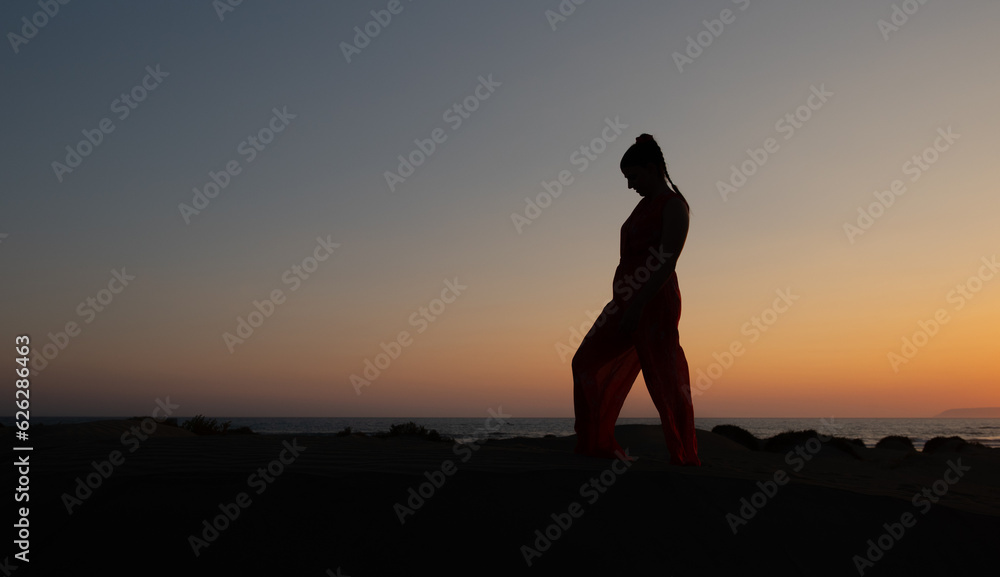 Silhouette of a woman dancing at a sandy beach at sunset. Caucasian woman posing outdoors at the coast.