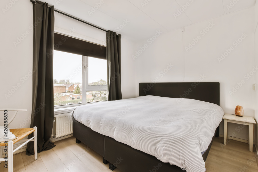 a bedroom with white walls and black curtains on the windowsilling there is a bed in front of the window a bedroom with white walls and black curtains on the windowsilling there is a bed in front of the window