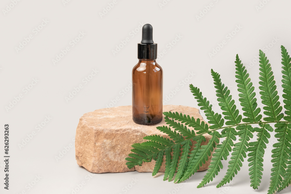 Dark amber glass bottle standing on stone. Natural skin care SPA beauty product design. Mineral organic oil cosmetics. Gray background. Mock-Up. Oily pipette. Face and body treatment. Front view stand