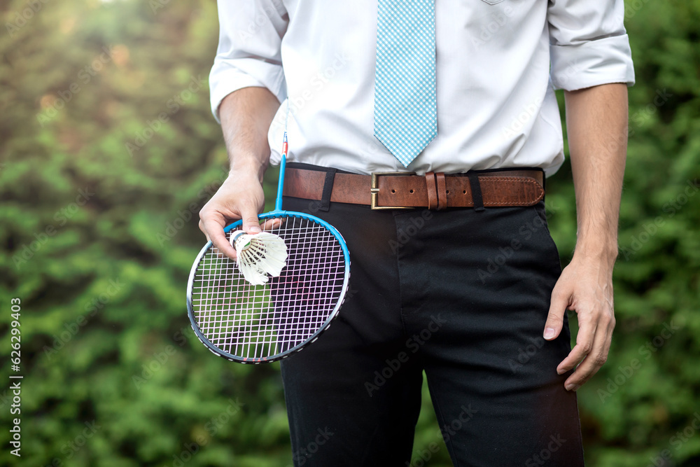Handsome man an in office clothes playing badminton outside during break. Mental health and healthy lifestyle concept
