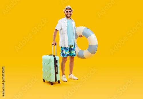 Full body photo of a funny young happy man tourist in rubber ring hurrying up on summer holiday trip in office clothes isolated on studio yellow background. Vacation and travel concept.
