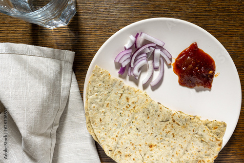 A tasty simple north Indian lunch with fenugreek roti or chapati, sliced red onion and spicy lime pickle, served on a plate on a wooden table. Top view. photo