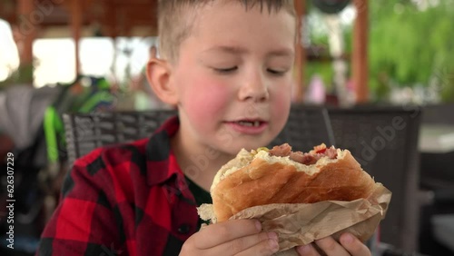 A child greedily eats a burger while walking in park. Close up portrait. Focus changing.
