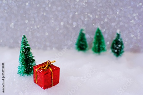 Christmas home decoration with Little handmade gift box in a snow covered miniature evergreen forest and bokeh light for copy space.