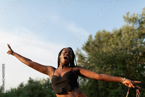 A young black woman with braids in her hair goofs around while taking a walk in the park at sunset