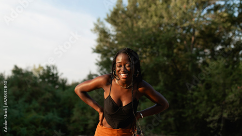 A young black woman with braids in her hair laughs during a walk in the park at sunset.