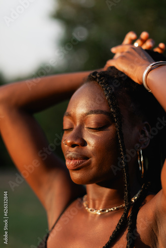 A young black woman with braids  touches her hair  feels beautiful  and enjoys the sun during a sunset stroll