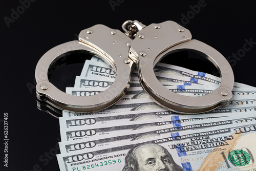 Handcuffs with cash money isolated on black background. Cash bail reform, bail bond and cashless bail concept. photo