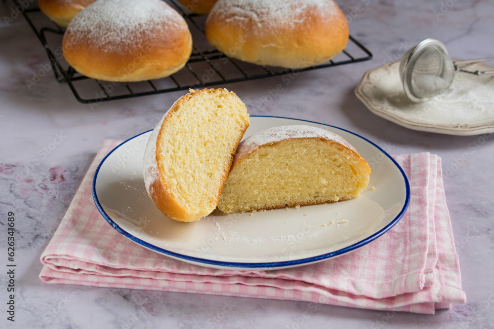 Sweet round buns with icing sugar on top cut in half on a white plate. Typical sweet from Majorca, Spain Sweet round buns with icing sugar on top cut in half on a white plate. Typical sweet from Majorca, Spain