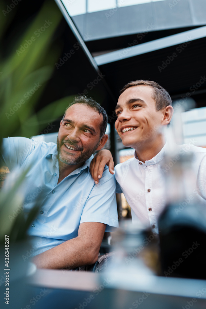 Handsome and happy father and his teenager son sitting in a restaurant and talking. Handsome and happy father and his teenager son sitting in a restaurant and talking.