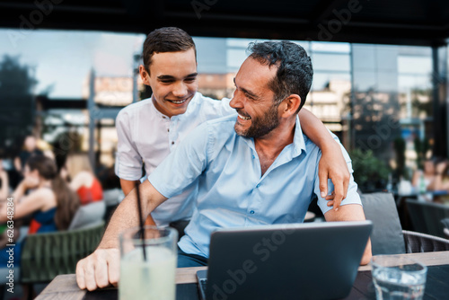 Handsome and happy father and his teenager son sitting in a restaurant and talking.