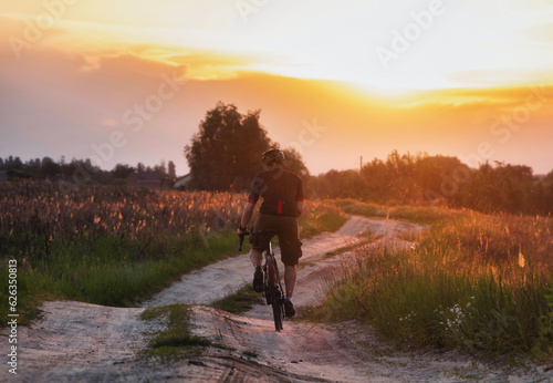 Cyclist riding a trail in a field on a gravel bike on a dramatic sunset background. Sport and active lifestyle concept.