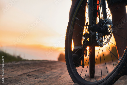 Closeup of bicycle front wheel on a trail against sunset background. Cycling outdoors.