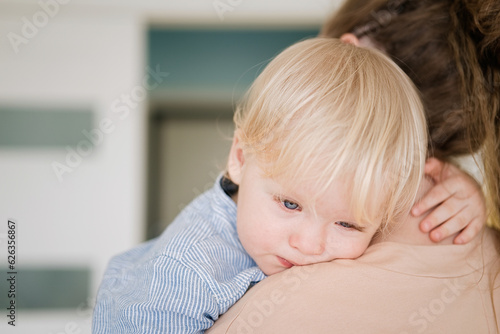 Fotografie Cute little upset baby boy weeping on mom's shoulder in his mother's arms, huggi