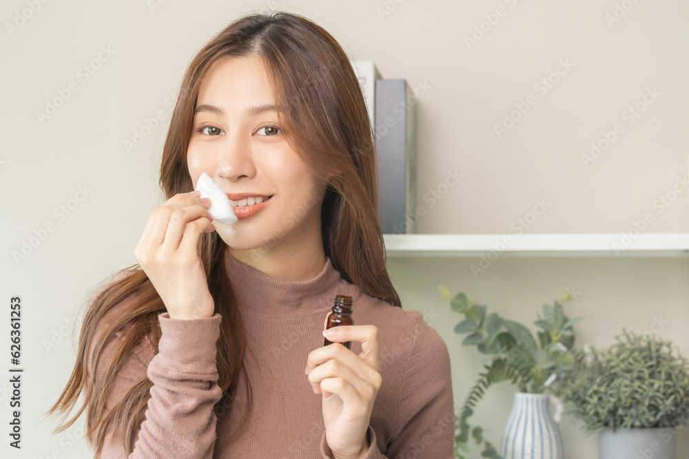 Aromatherapy, cute asian young woman holding cotton pad, bottle of essential perfume oil, enjoying smell fragrance of herbal from medicine natural organic at home. Therapy treatment, beauty skin care.