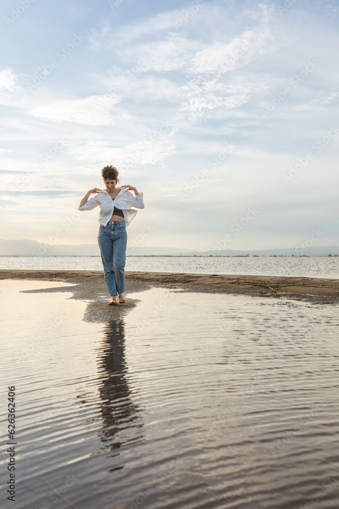 woman on the beach dancing at sunset in backlight with the sun behind in shadow, woman on vacation walking on the sand with golden water reflections from the sun at sunset