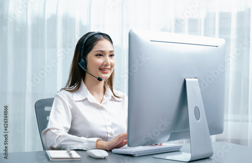 Foto Asian call center with headset and microphone working on her laptop