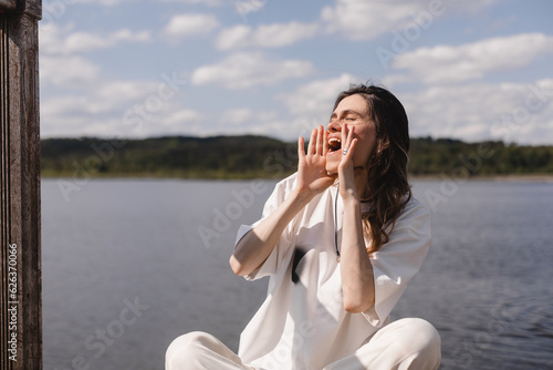 Happy woman hold hands near mouth and shout of freedom, scream call her friends. Woman look happy and  joyful. Emotional recovery, traveler girl rest in the lake. © zvkate