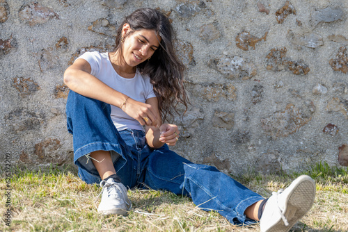 Photos Jeune femme assise dans l'herbe contre un mur dans ses pensées