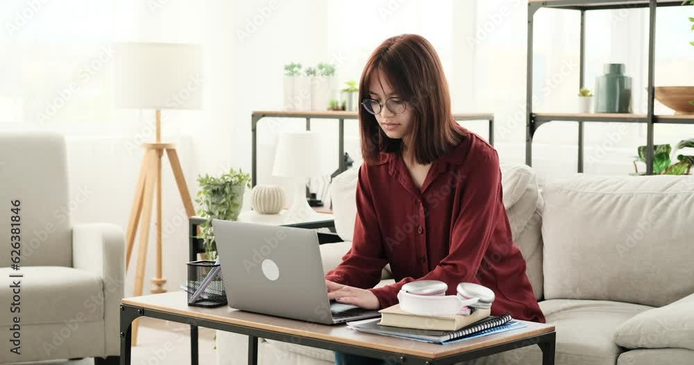 Engrossed in her work, a teenage girl sits on the couch in the living room, typing on her laptop. With a focused expression and determined posture, she channels her concentration into her tasks.