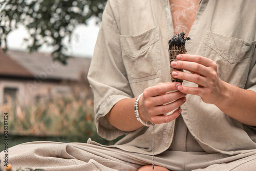 Woman Inhaling Incense Smoke During Meditation.Ground level of relaxed female meditating and breathing while sitting in Lotus pose near fragrant incense during yoga session in garden
