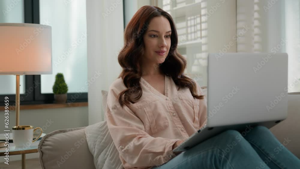 Caucasian woman girl relax sitting on couch at home sofa using laptop computer typing message happy lady chatting browsing surfing internet social media studying working online looking at camera smile Caucasian woman girl relax sitting on couch at home sofa using laptop computer typing message happy lady chatting browsing surfing internet social media studying working online looking at camera smile